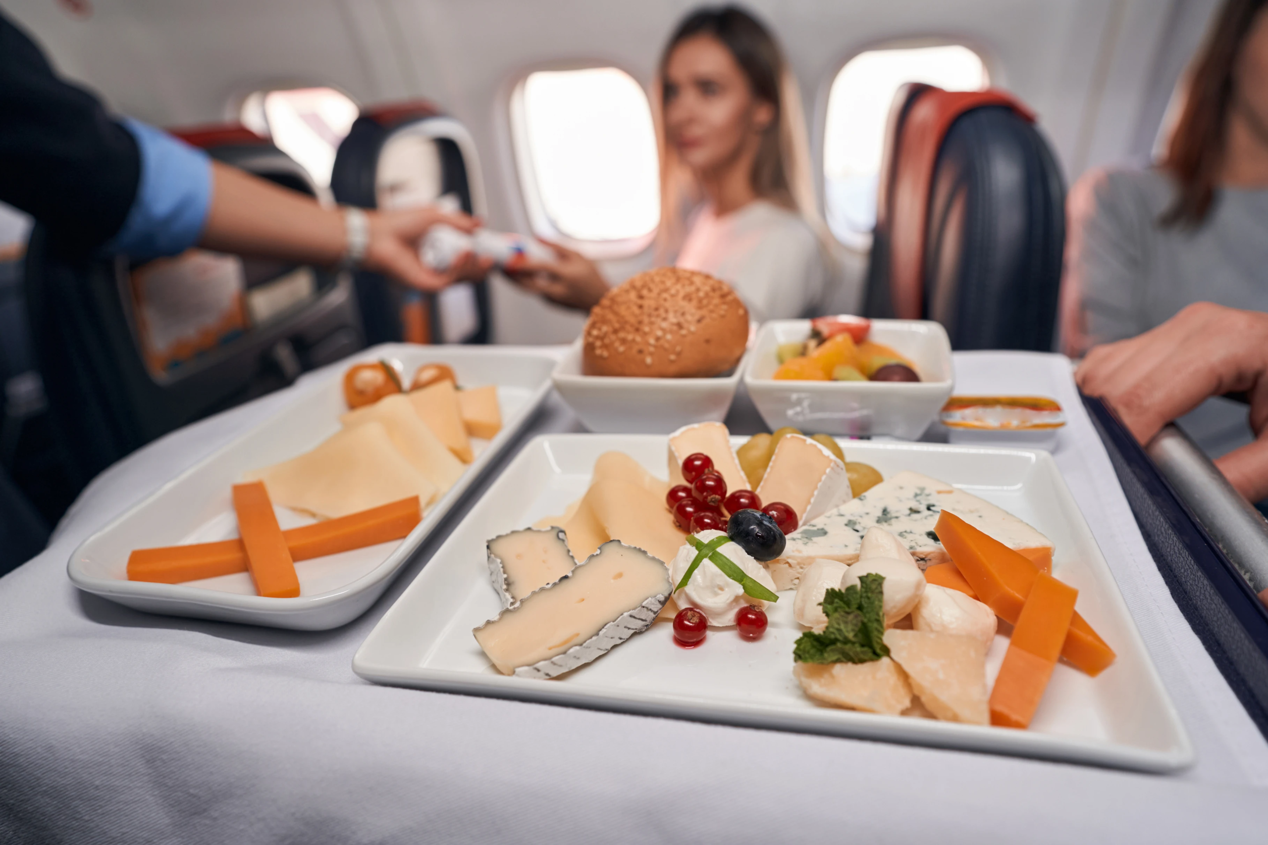 Weiße Tabletts mit Burger, Käse, Möhren und Beeren auf einem Servierwagen im Flugzeug