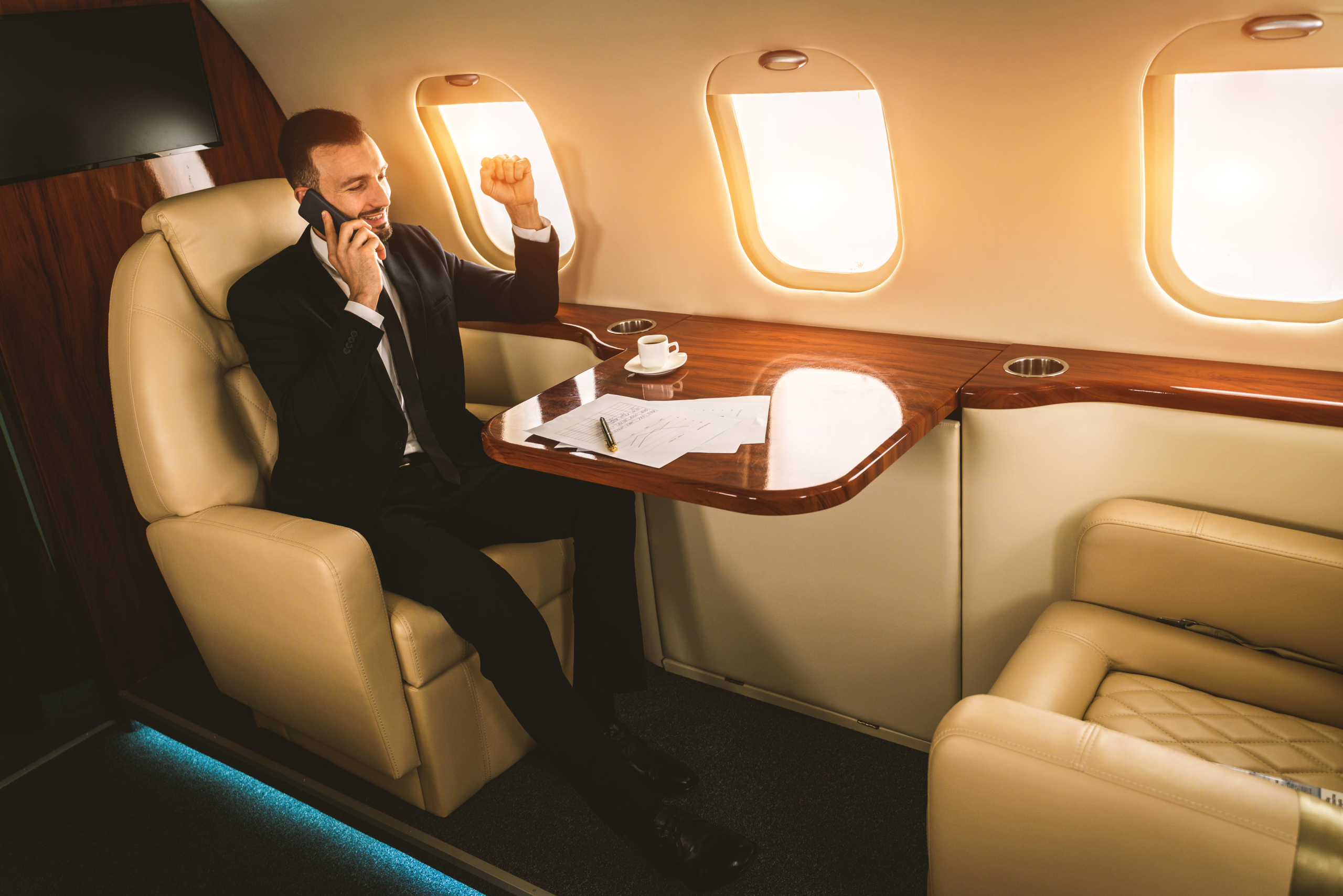 Gutaussehender Geschäftsmann in elegantem Anzug, der in einem exklusiven Privatjet fliegt – Erfolgreicher Unternehmer in der exklusiven Business Class eines Flugzeugs, Konzepte rund um Wirtschaft und Transport